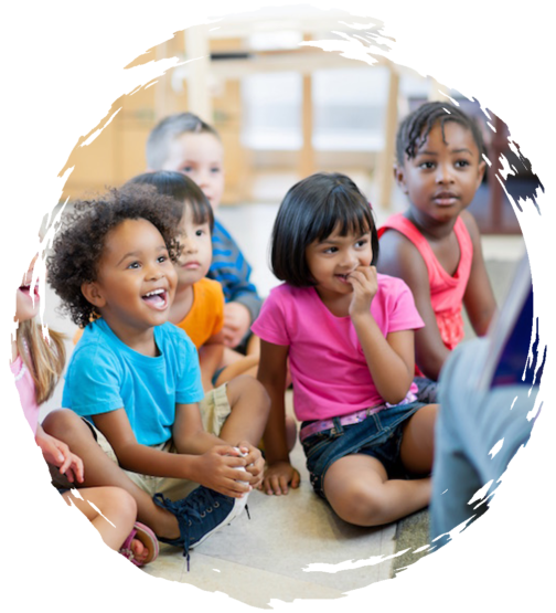 Preschoolers sitting on the floor smiling and listening to their teacher